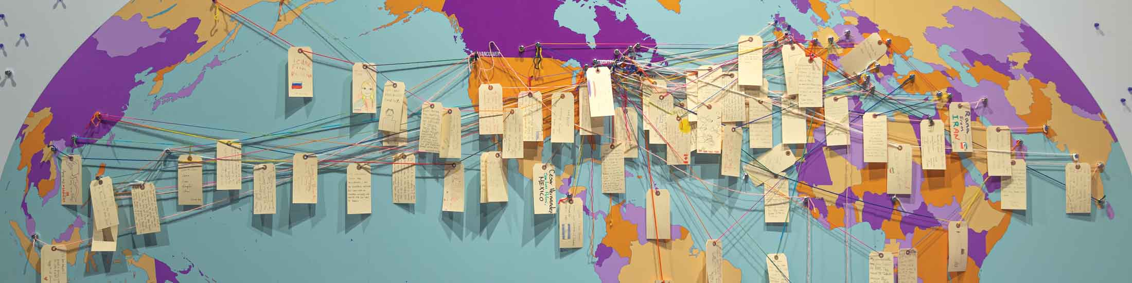 Luggage tags with visitors notes are attached with string on a large map of the world.