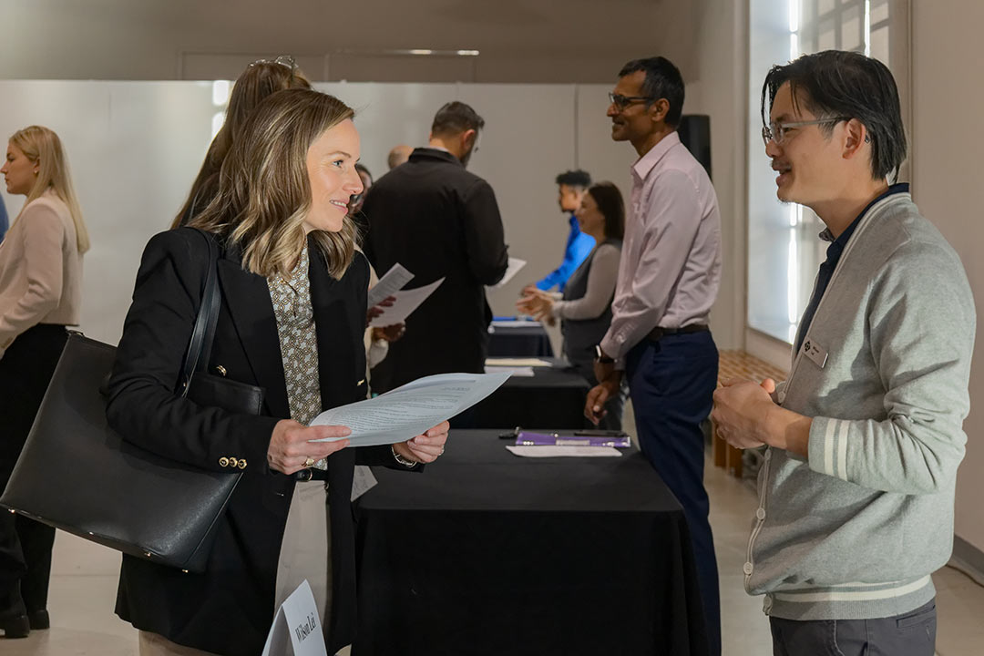 An Asian man speaking to a recruiter at a networking table during an Employee Showcase event with other job seekers and employers in the background.