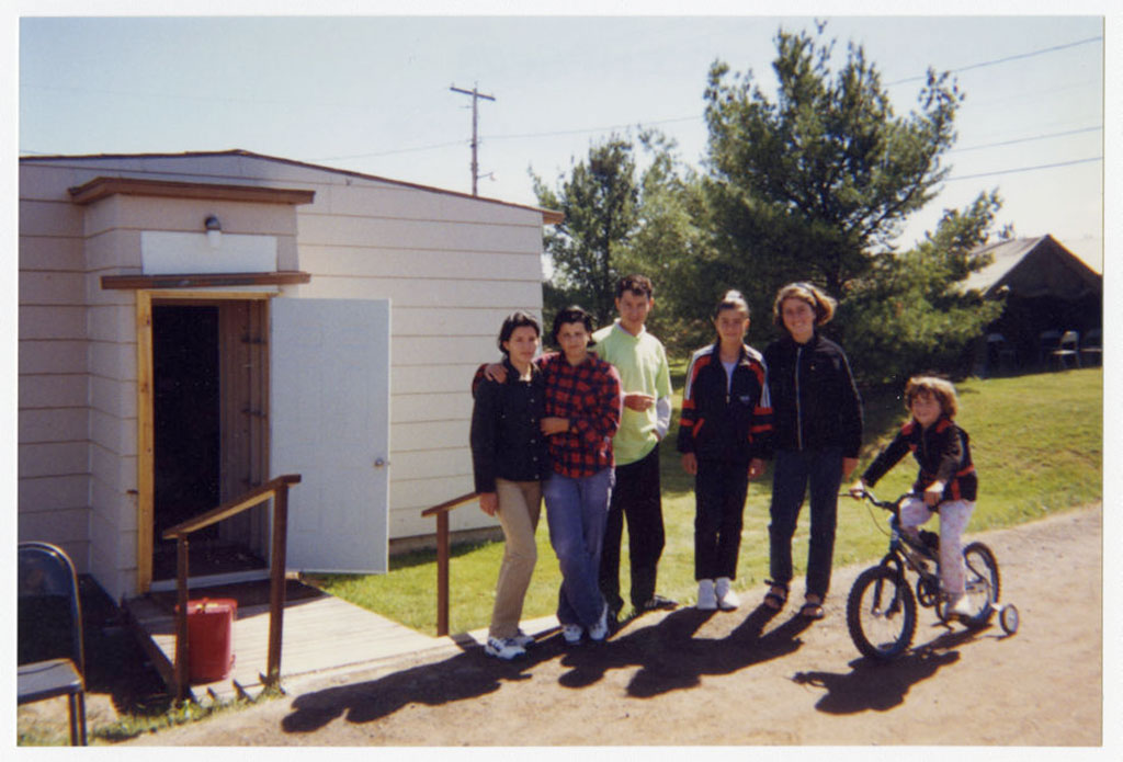 A group of people and a girl on a bicycle are grouped outside a white building.