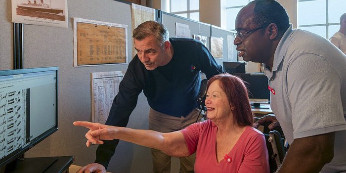 A museum staff member shows delighted visitors something on a computer screen.