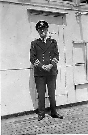 A man is standing in front of a door of a ship and he is wearing a captain's uniform.