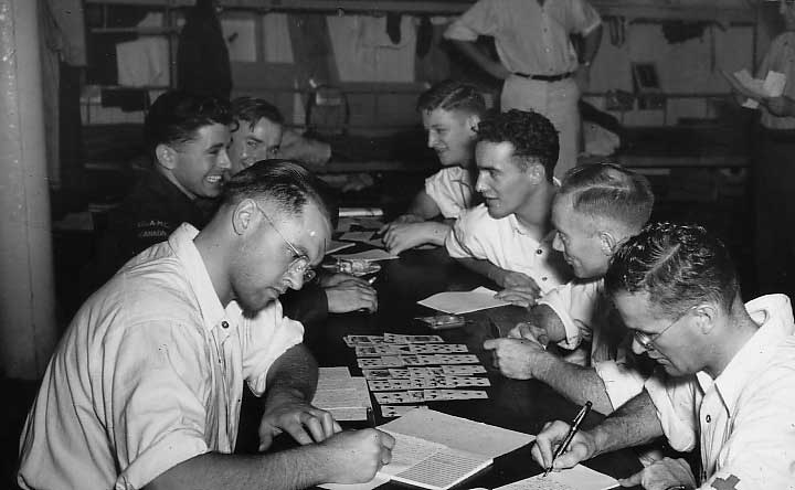 Group of young men sitting around a table playing cards and writing on a board.