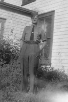 Man wearing military clothing with glasses is standing in front of a window.