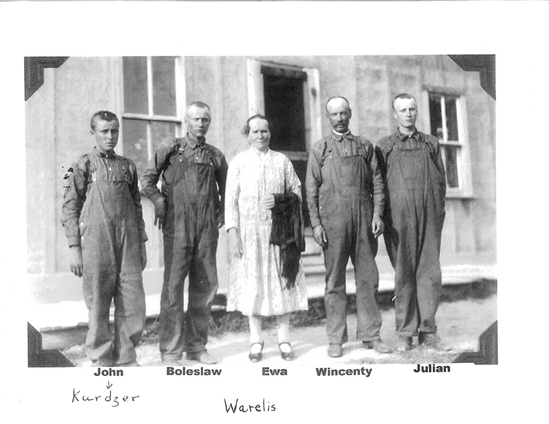 Four men in construction uniform and a woman in white dress standing in front of building.