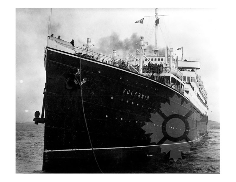 Black and white image of MS Vulcania at anchor, seen close up from the bow, with passengers visible on deck.