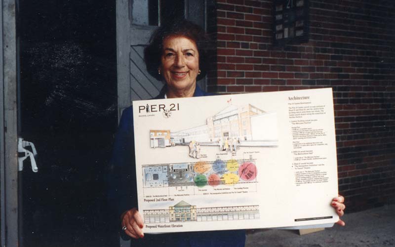 A woman is hold up a large floor plan drawing.