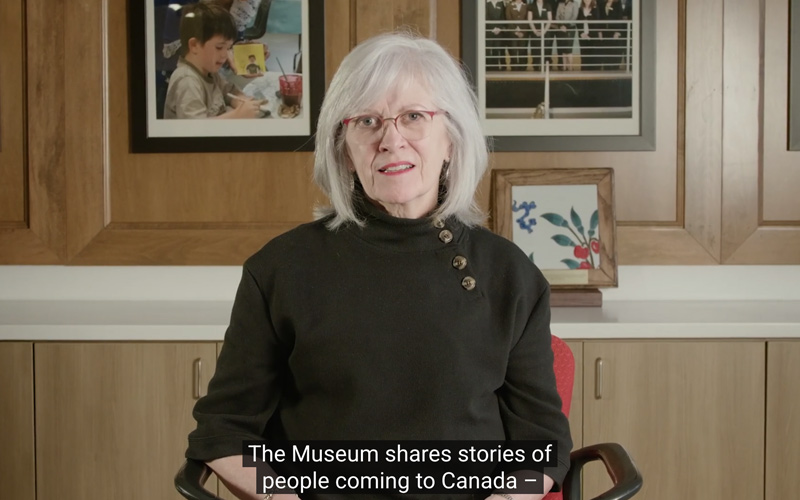A screenshot of the Annual Public Meeting video where a white woman, interim CEO Michele Mckenzie, sits in a boardroom.