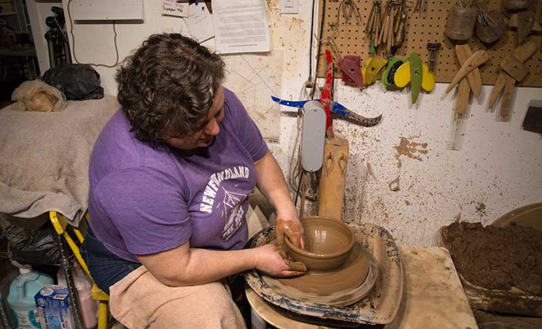 Woman in black tee shirt works on molding another piece of pottery on the wheel.
