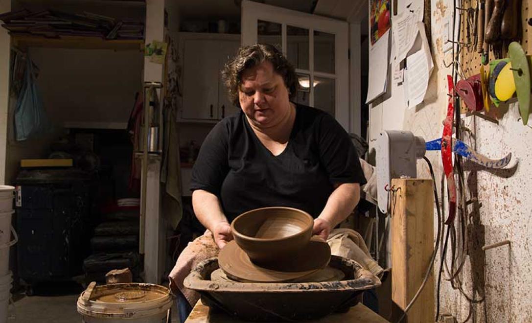 Side view showing woman forming clay pottery on a wheel.