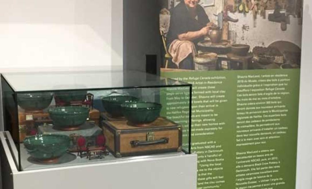 Glass display case with pottery bowls inside and a banner stands next to it with an image of the artist who created the bowls.