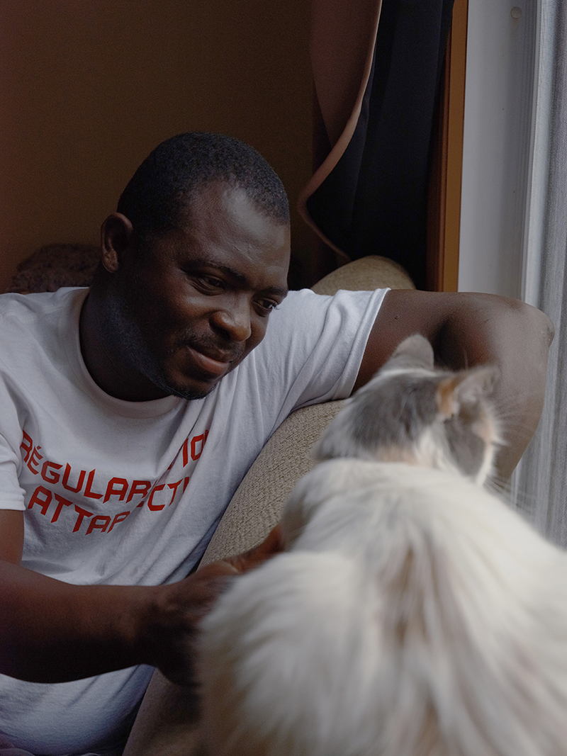 A man in a white tee shirt sits and plays with a fluffy-haired cat.
