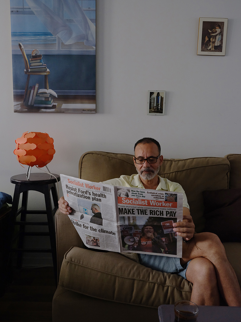 A man sits on a couch while reading a newspaper.