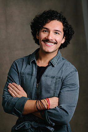 A portrait of Santiago Guzmán smiling at the camera with his arms crossed.