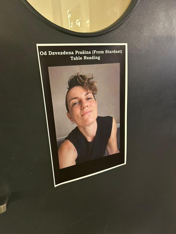 A poster on a black wall for Annie Valentina’s table reading event, featuring a picture of Annie.