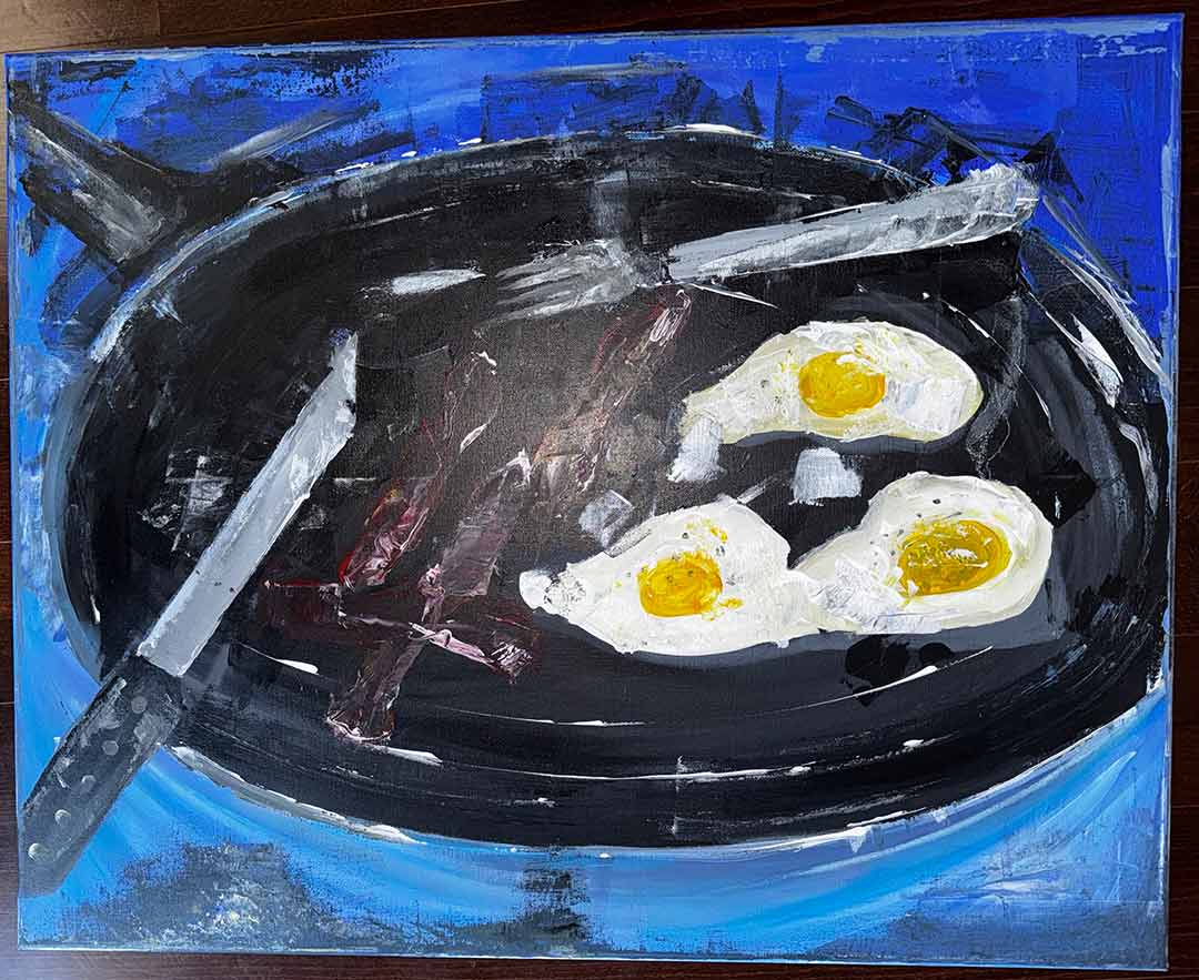 Bacon and eggs in a black frying pan with a knife and fork on a blue background.