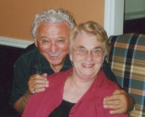 A man and woman pose with his hands on her shoulders.