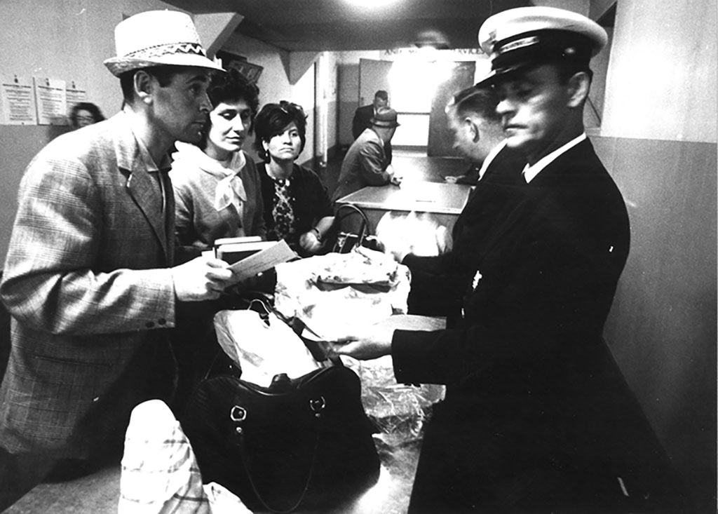 An immigration officer inspects the contents of a suitcase, as the passenger looks on.