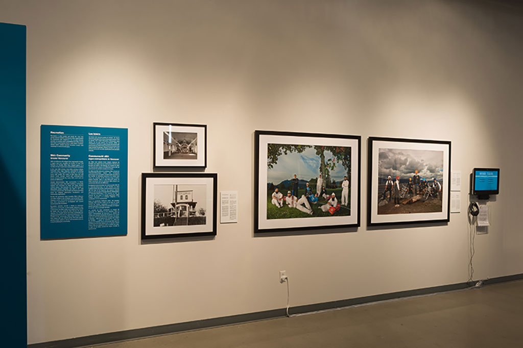 A long wall with several framed portraits hanging, as well as teal plaques with text.