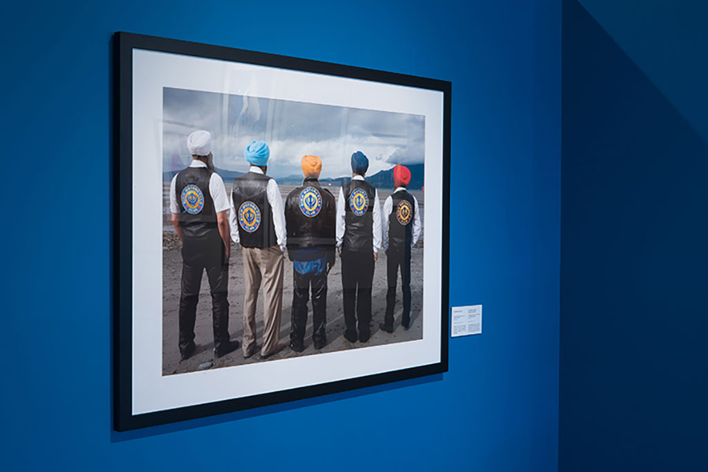 Five men wearing turbans and leather jackets are standing with their backs to the camera, looking into the distance.