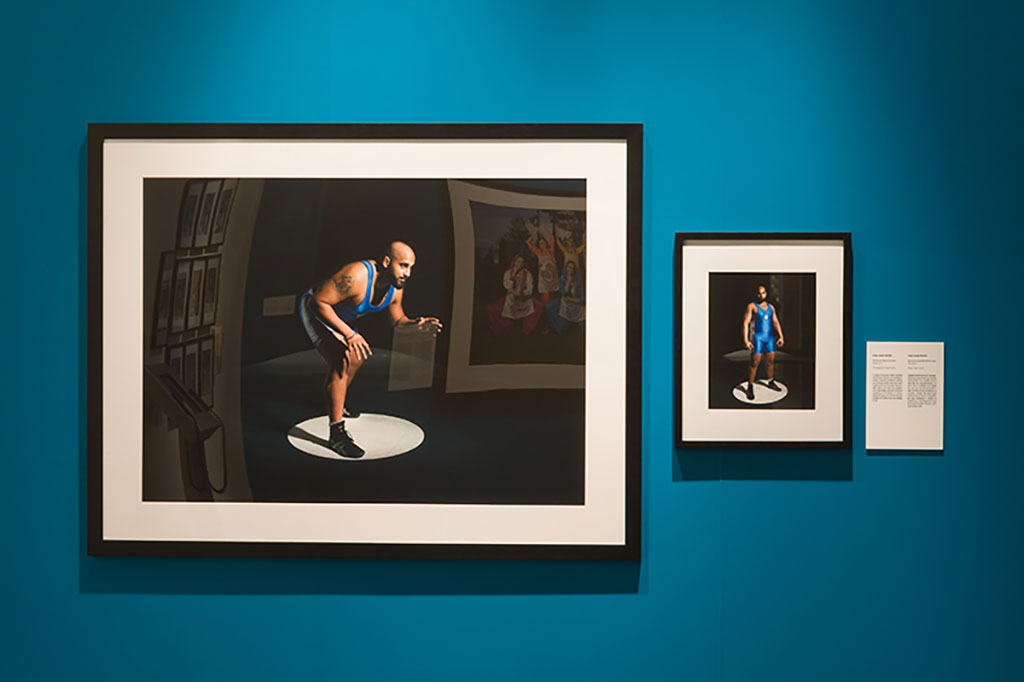 A large and smaller portrait hang on the wall, both depicting a young male wrestler in wrestling stances.