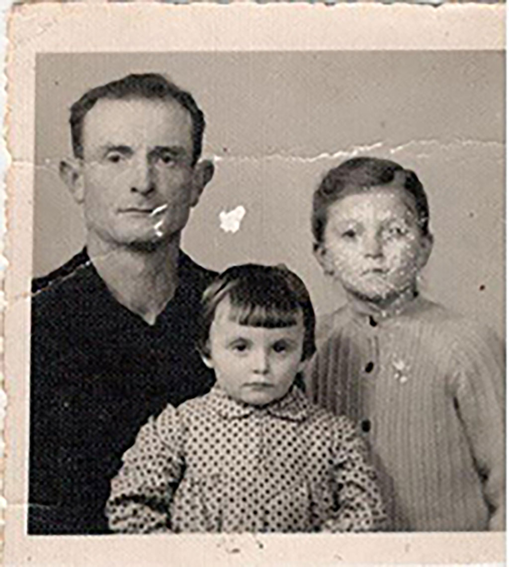 Old cracked photo showing man in black sweater seated next to small boy and small girl.