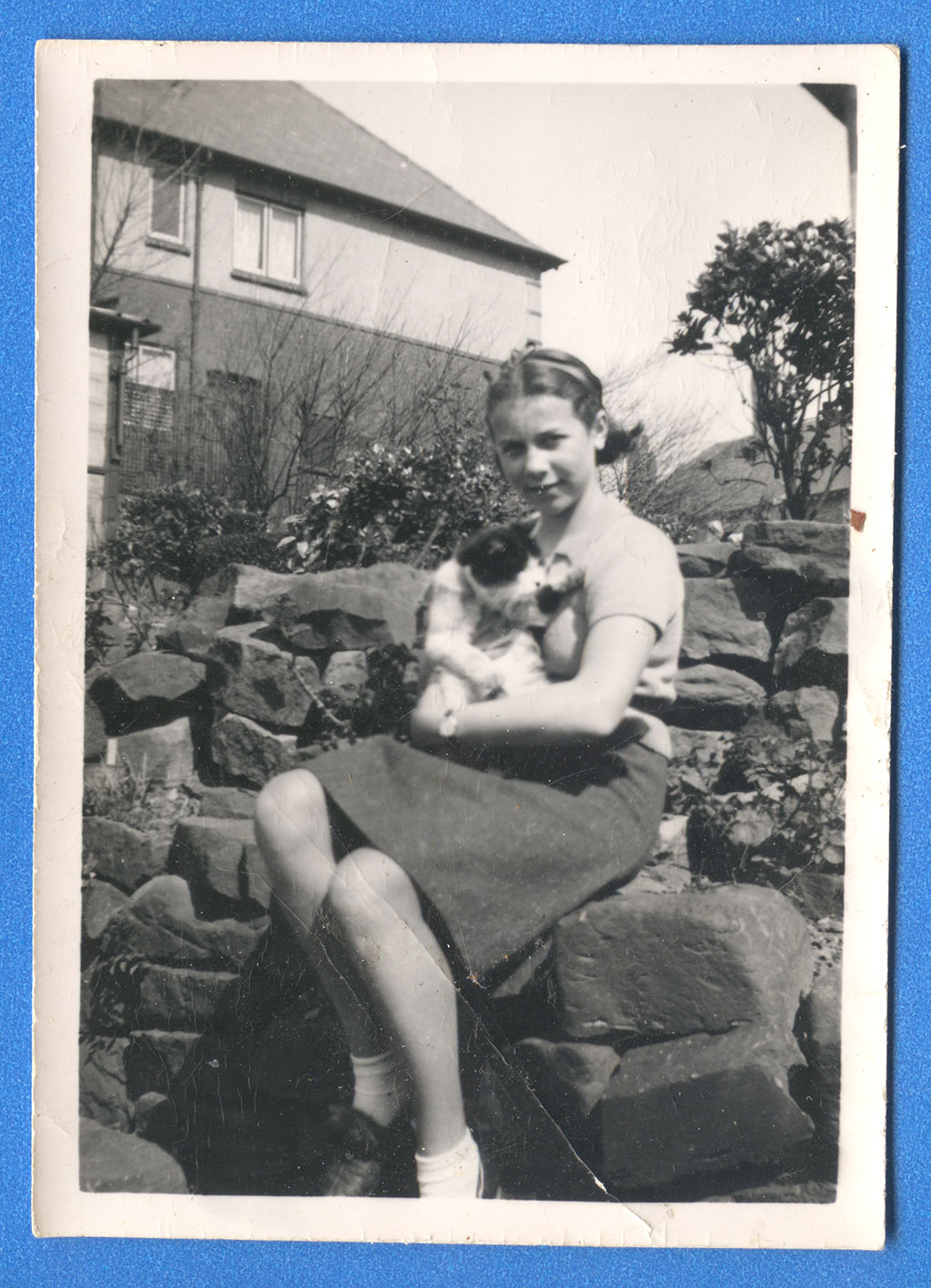 A young woman is sitting on a rock wall, holding a cat in her arms.