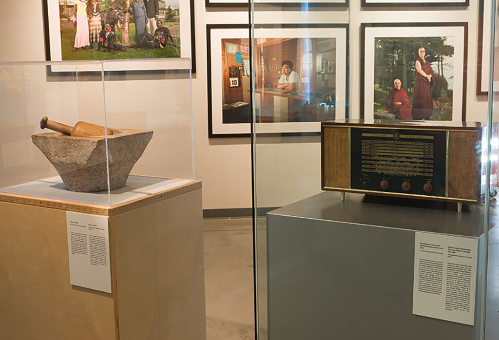 Two artifacts in glass cases in the middle of an exhibition room, framed portraits are seen in the background.