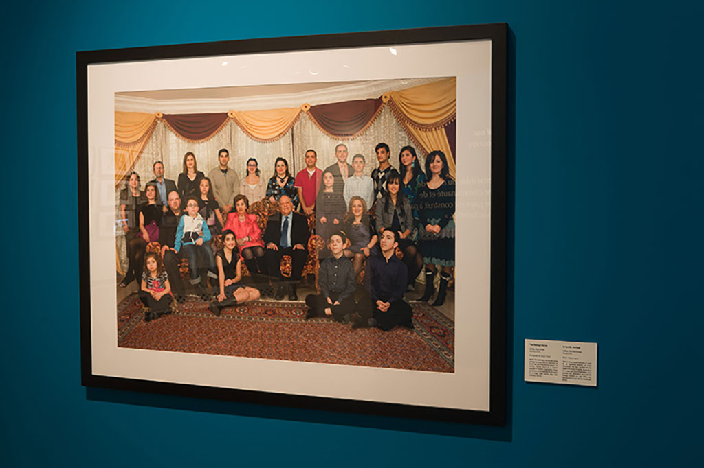 A beautiful coloured portrait of a large family hangs on a teal-coloured wall.