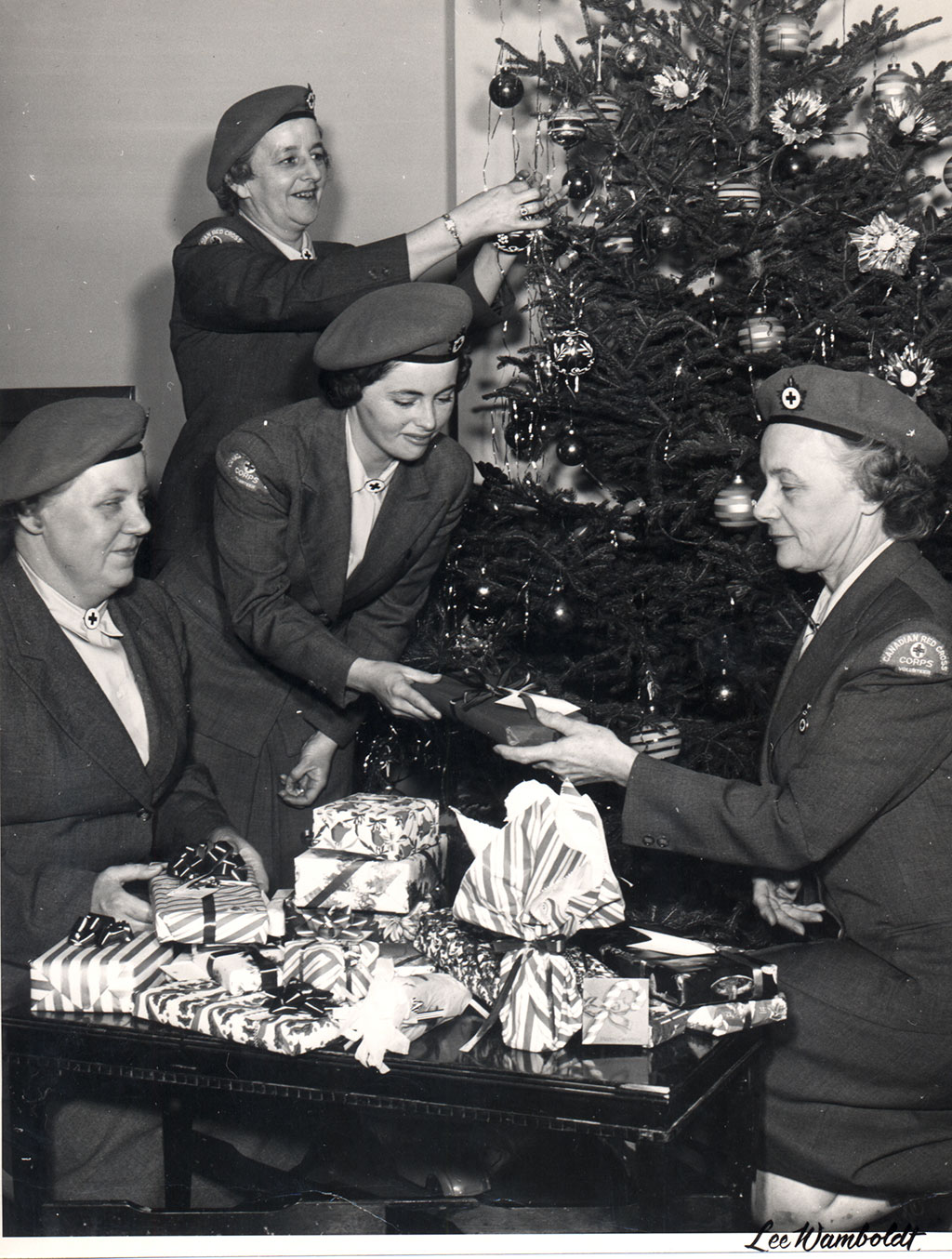Women in uniforms decorate a Christmas tree and wrap gifts.