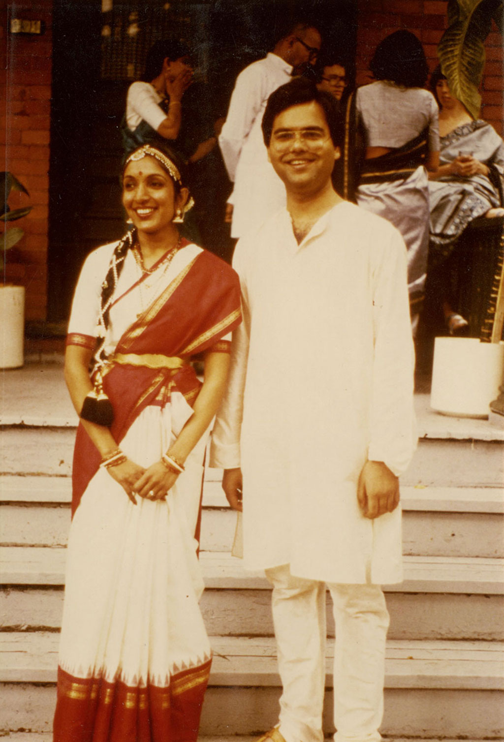 A young couple in traditional Indian clothing stand together, smiling.