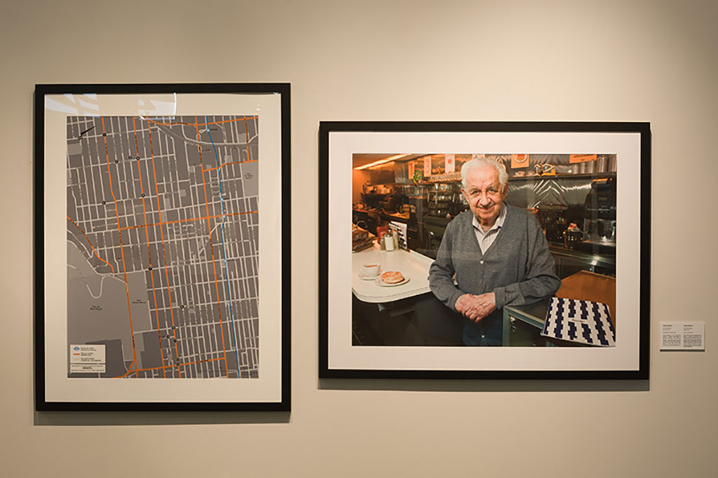 Two framed images hanging on a wall; one shows a street grid and the other is a man smiling as he stands at the counter of a restaurant.