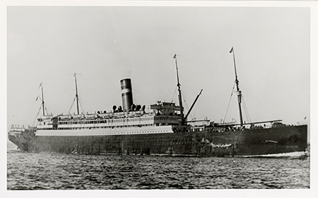 A large ship with four masts, passengers visible on the deck.