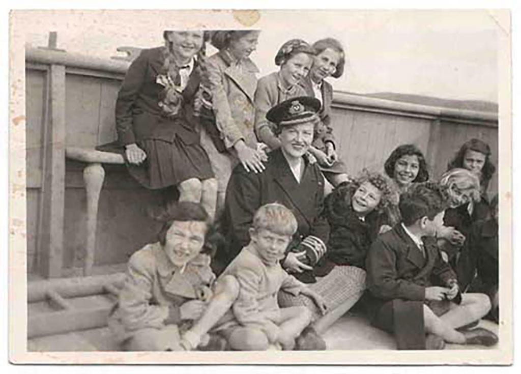 A woman is seated with children of varying ages standing and sitting around her.