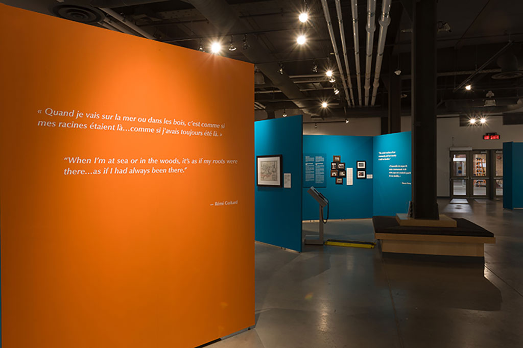 An exhibition room with large orange and teal panels containing images and text hanging on them.