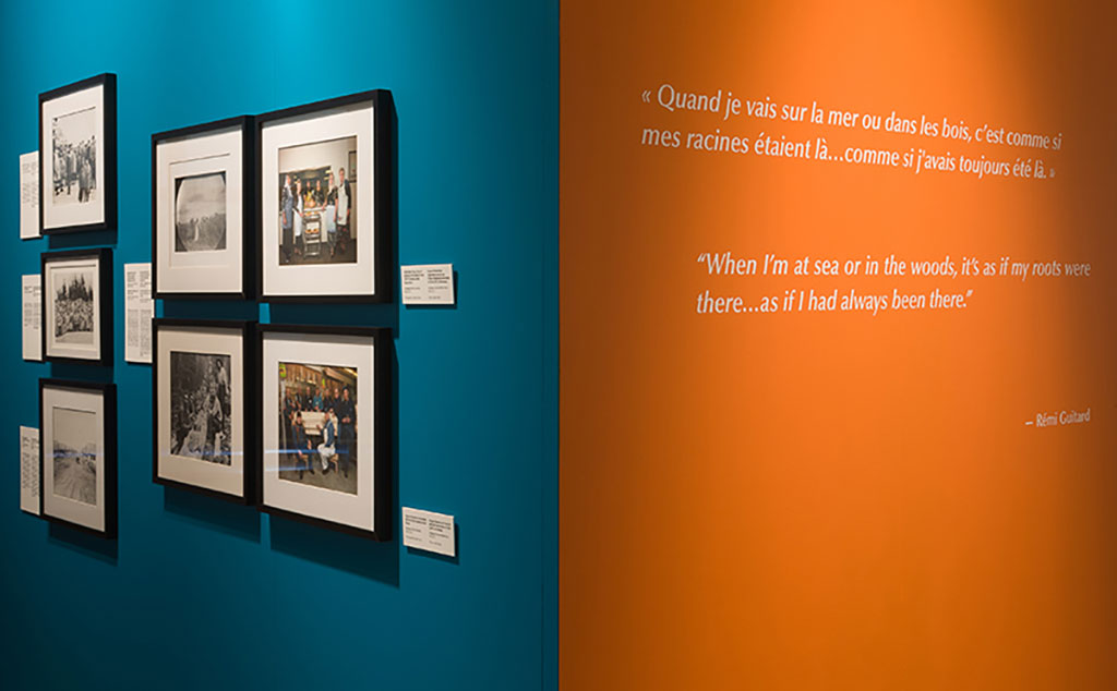 An exhibition room with large orange and teal panels containing images and text hanging on them.