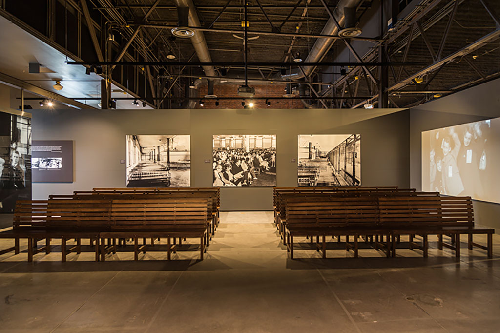 Rows and rows of benches can be seen facing a wall with black and white images projected onto it.