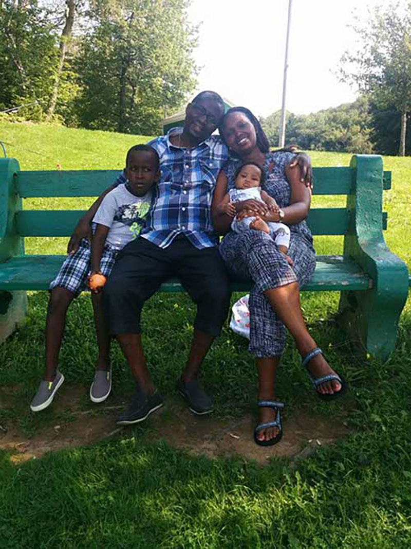 Angelique and her family sitting on a park bench on a sunny day.