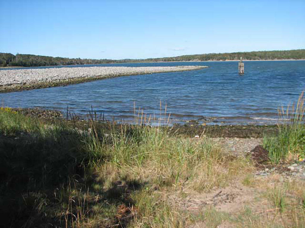 Stone-laden land juts out into a body of water, with waves lapping the shore.