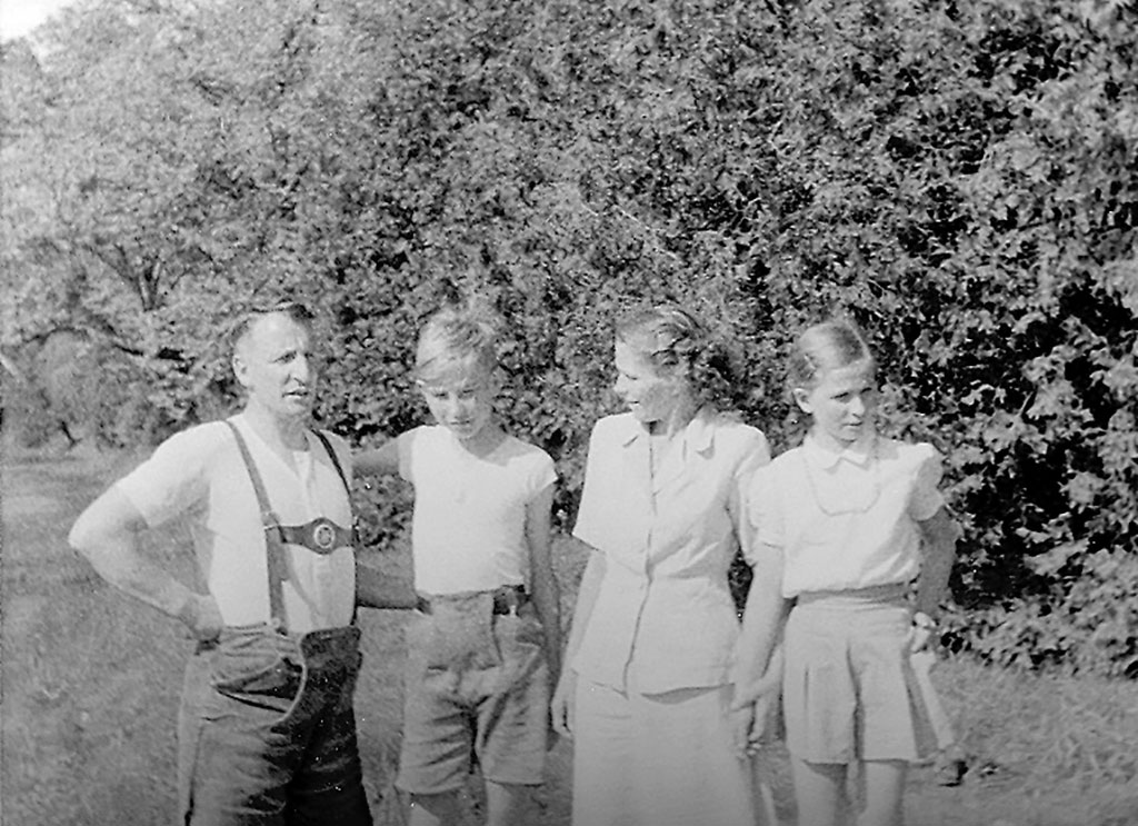 A black and white photograph of the Schlechta family of four standing casually in a row in a park with a backdrop of trees.