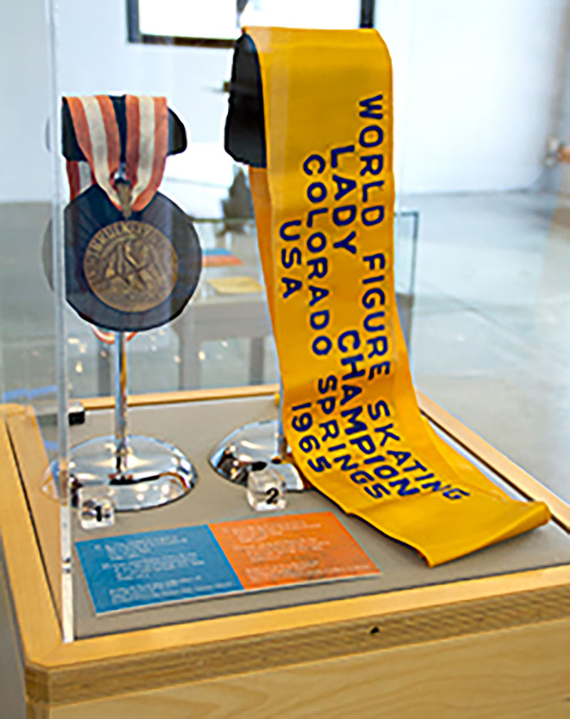 An Olympic bronze medal sits inside a glass case as part of a larger museum display.