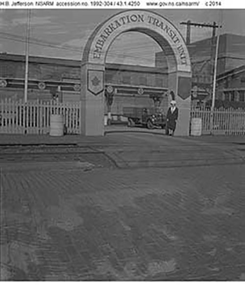 A man is standing below a cement archway that reads Embarkation Transit United.