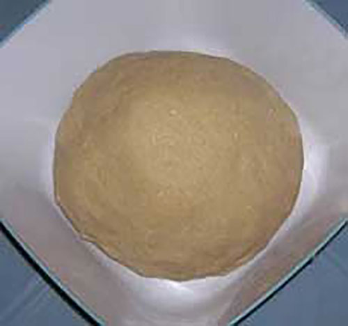 Round mass of bread-like substance sitting on a square white plate.