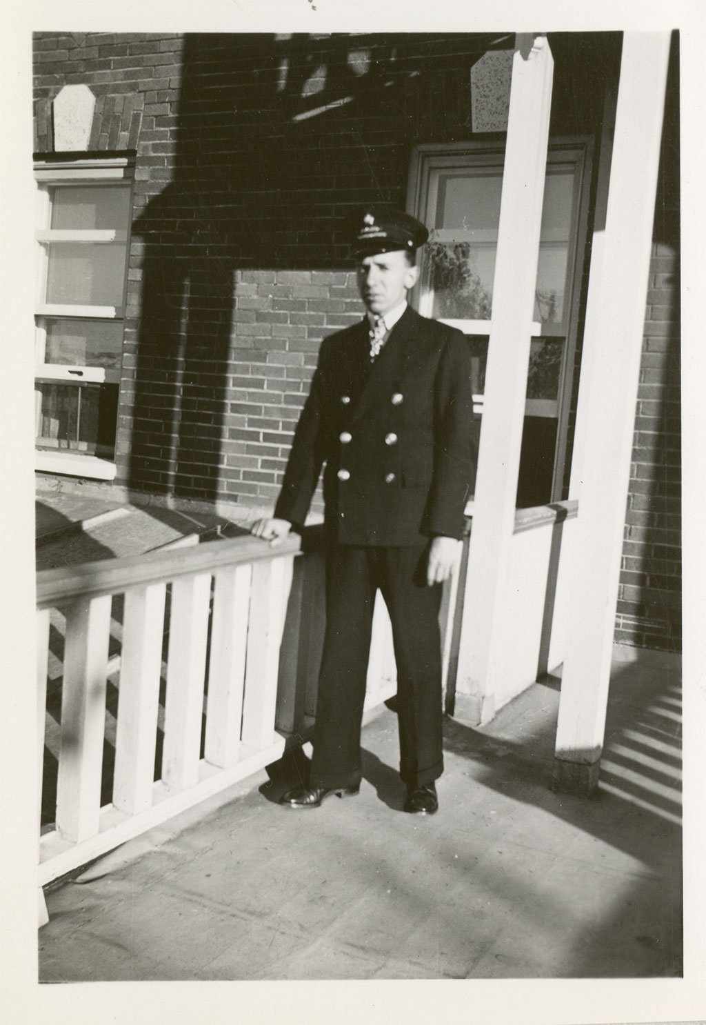 A man in hat and uniform stands with his hand on a wooden railing as he looks at the camera.