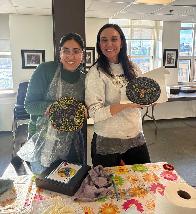 An Indian woman and a white woman hold up finished mosaic art pieces.
