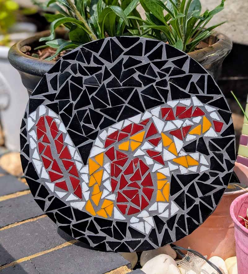 A circular mosaic panel of a beaver in red, white, and orange glass tiles against a black background.