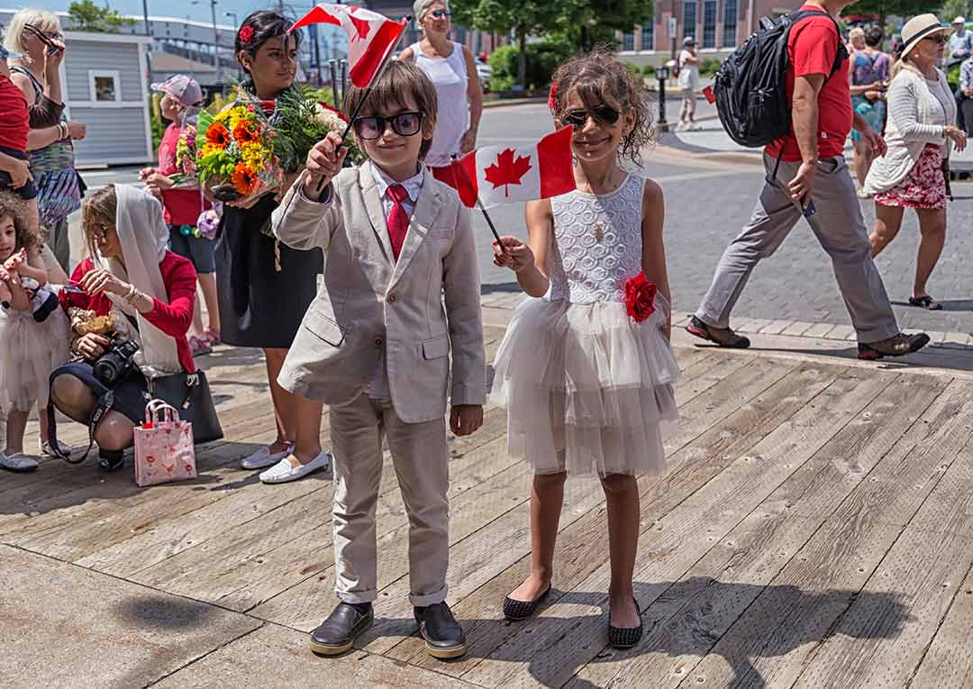 Two children waving Canadian flags stand outside the Museum.