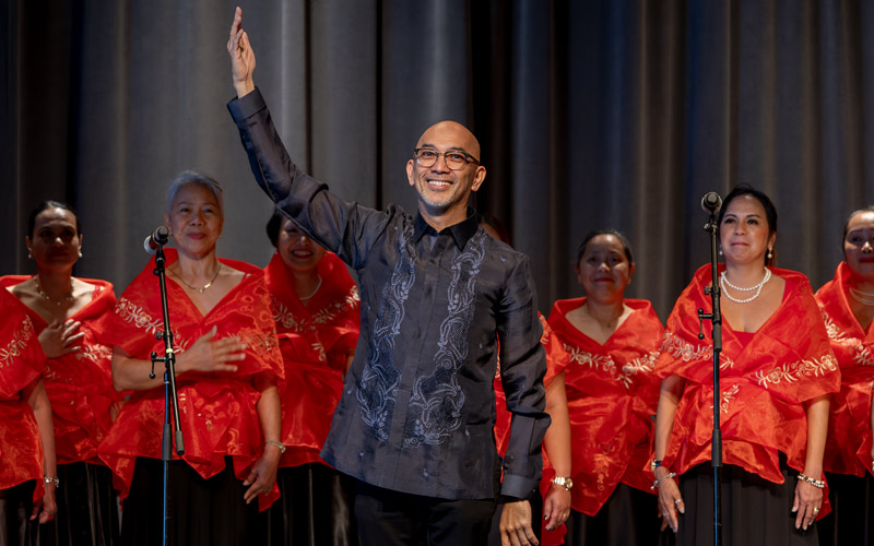 A group of Filipino women in red garments smiling behind a bald Filipino man.