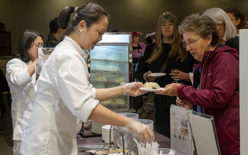 A Filipino woman in a white chef’s jacket serves a plate of food.