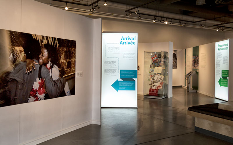 An image of the exhibition, featuring a photograph of two people hugging, text panels, and a glass display case with objects.