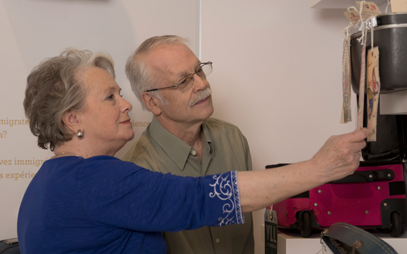 Two people look at a luggage tag on a piece of luggage displayed on the wall.